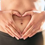 woman holding hands in a heart over stomach to depict body image and mental health