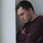 Man with his arms crossed standing in a corner depressed