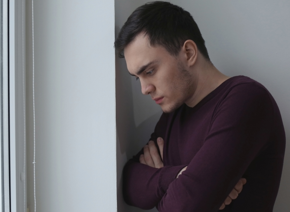 Man with his arms crossed standing in a corner depressed