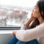 Woman looking out the window durnig the winter suffering from seasonal depression