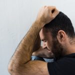 Sad bearded man standing against a wall with his hands on his head depressed