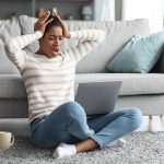 Woman sitting on the floor stressed online shopping during the holidays