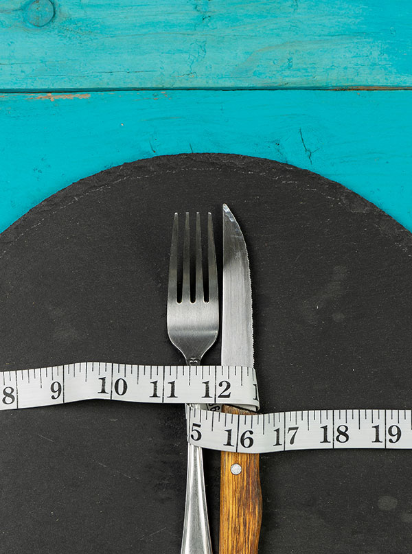 knife and fork on a plate wrapped by measuring tape