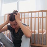 Mother sitting next to her child's crib dealing with postpartum anxiety