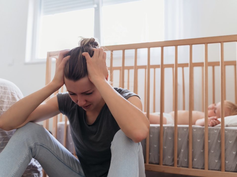 Mother sitting next to her child's crib dealing with postpartum anxiety