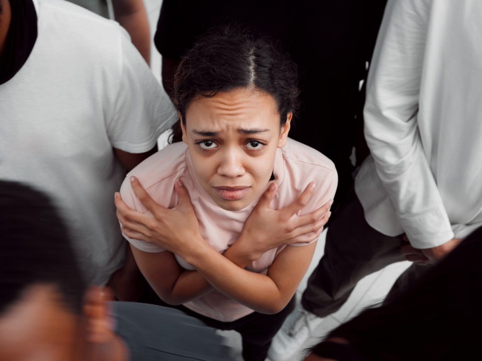 young adult woman standing in a crowd uncomfortable with her arms crossed over her chest