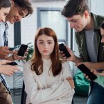 Teen girl sitting surrounded by other teens cyberbullying