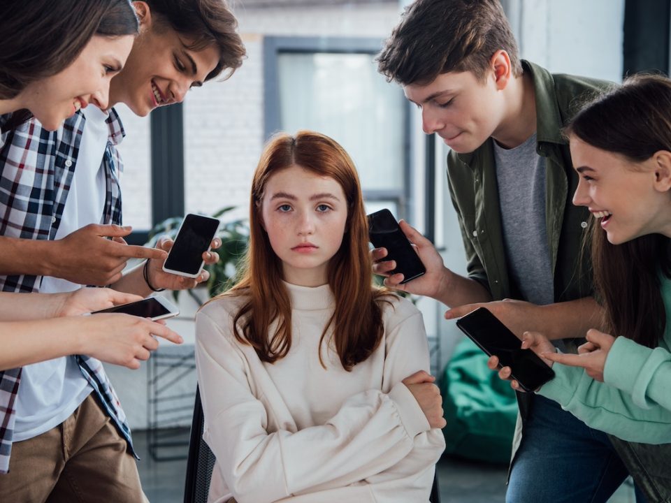 Teen girl sitting surrounded by other teens cyberbullying