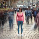 woman suffering from social anxiety standing alone as people blur around her