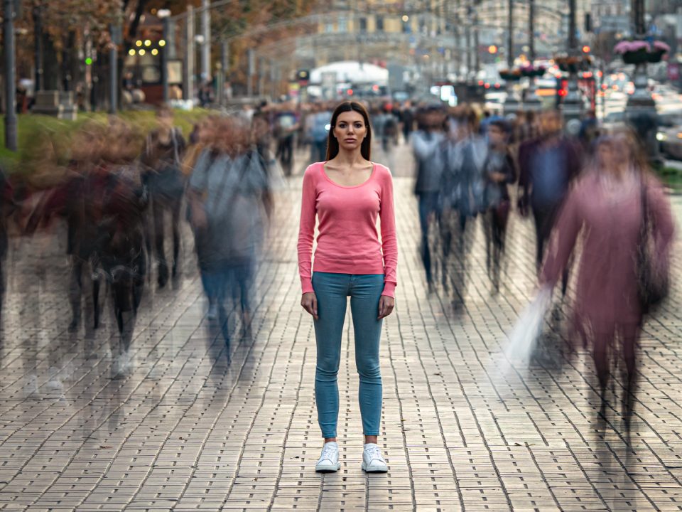 woman suffering from social anxiety standing alone as people blur around her