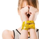 Woman standing with her hands bound by measuring tape to depict bulimia nervosa