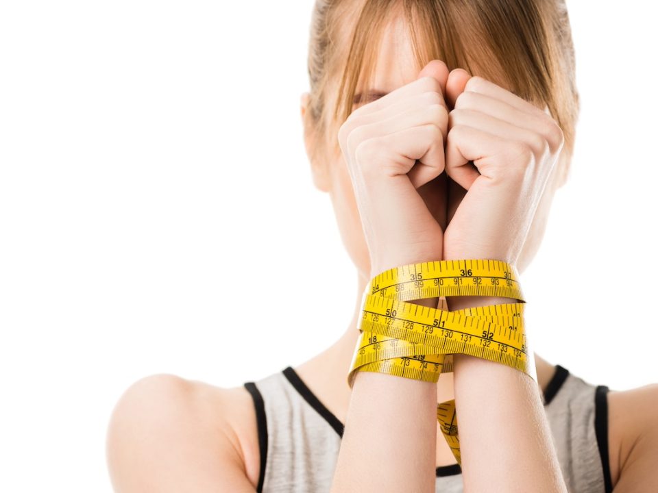 Woman standing with her hands bound by measuring tape to depict bulimia nervosa