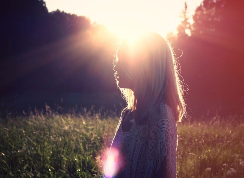 young adult woman standing in a sunny field hopeful about mental health