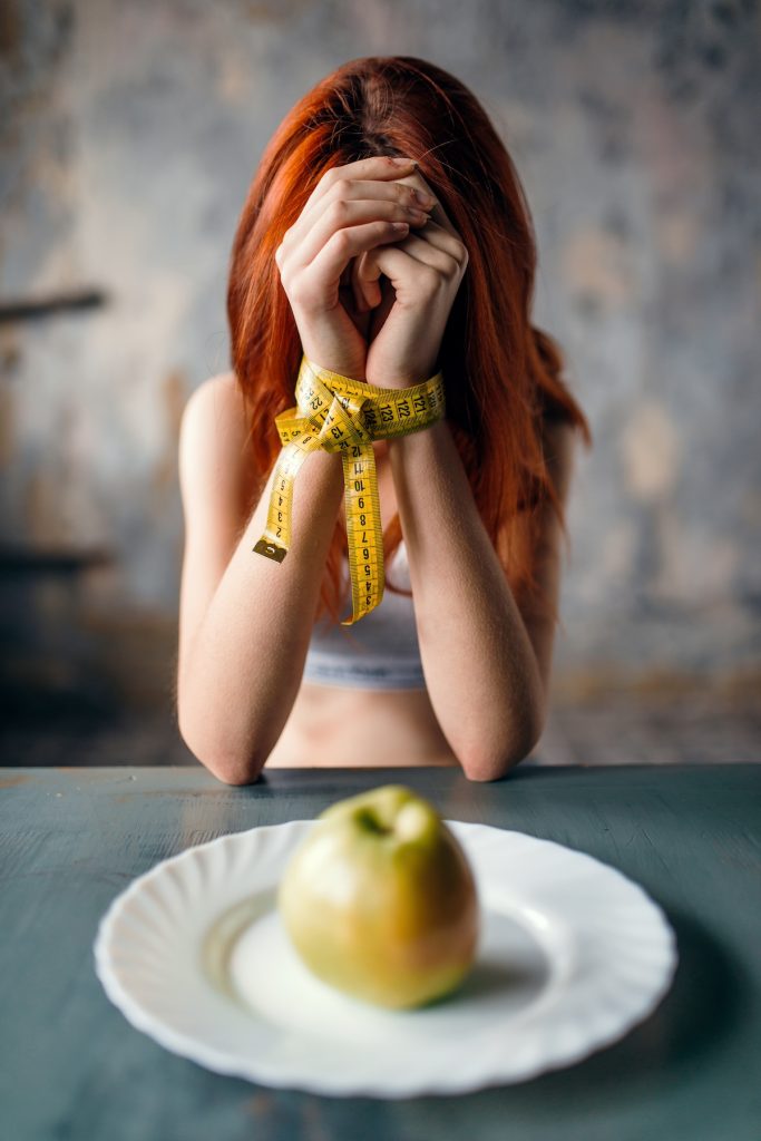 woman sitting at a table with hands tied by measuring tape with an apple in front of her